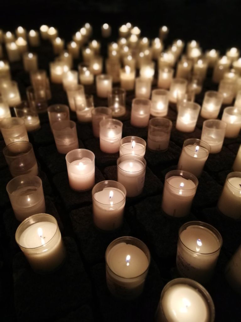 This is a picture of a bunch of lit candles on the floor in the dark. 
